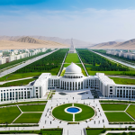 **

"A wide, panoramic shot of Ashgabat, the 'White Marble City', Turkmenistan, during the daytime. Show modern architecture gleaming in the sun, with parks and green spaces visible. In the background, rolling hills or desert landscape. The image should convey a sense of modern elegance and peacefulness. Fully clothed people are strolling through the parks. Safe for work, appropriate content, professional architecture photography, perfect anatomy, natural proportions, family-friendly."

**